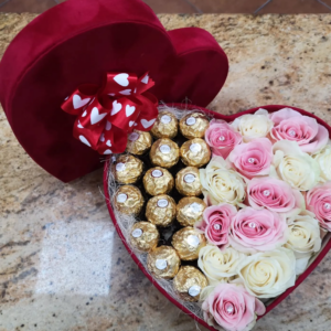 Caja en forma de corazón decorada con rosas rosadas y blancas en un lado, y bombones Ferrero Rocher en el otro, con una tapa de terciopelo rojo y un lazo con corazones blancos.