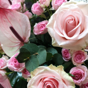 Detalle de un ramo de rosas en tonos rosados suaves, con hojas decorativas blancas caladas y un fondo de flores en tonos pastel.