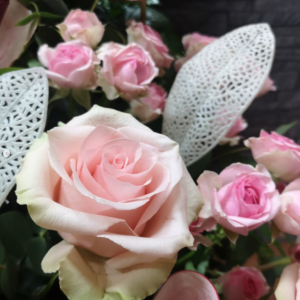 Detalle de un ramo de rosas en tonos rosados suaves, con hojas decorativas blancas caladas y un fondo de flores en tonos pastel.