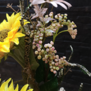 Detalle de un arreglo floral con un girasol amarillo brillante, bayas decorativas en tonos crema y rosa, ramas texturizadas y flores silvestres.