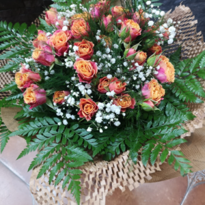 Ramo floral con rosas melocotón de bordes rosados, combinadas con delicadas flores blancas de paniculata y un fondo de hojas verdes brillantes en un diseño elegante y armonioso.
