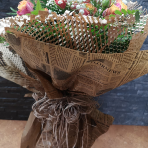 Ramo de flores envuelto en papel kraft con diseño de periódico y decorado con un lazo rústico de cuerda natural, con un fondo oscuro que resalta su presentación.