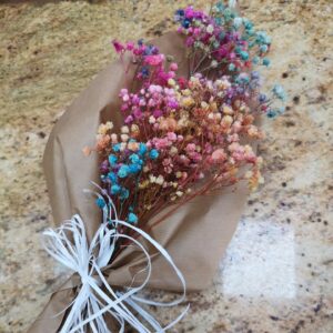 Ramo de flores secas teñidas en colores vibrantes como azul, rosa, naranja y morado, envuelto en papel kraft con lazo blanco.