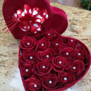 Caja en forma de corazón con rosas rojas decoradas con pequeños diamantes en el centro, acompañada de un lazo rojo con corazones blancos.
